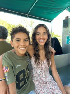 A brother and sister sit with arms around each other on a boat.
